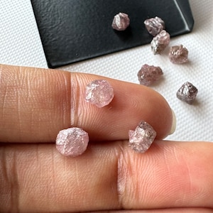 May include: A collection of small, rough, pink and gray diamonds. The diamonds are faceted and have a natural, unpolished look.