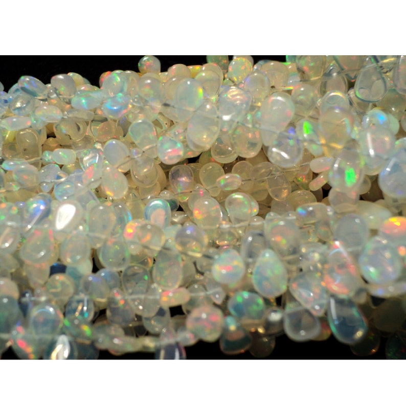 May include: A strand of white opal gemstone beads with iridescent rainbow flashes. The beads are oval shaped and have a smooth, polished finish.