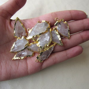 May include: A group of clear quartz arrowhead pendants with gold-plated edges. The pendants have a raw, natural look and are perfect for jewelry making.