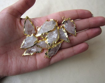 May include: A group of clear quartz arrowhead pendants with gold-plated edges. The pendants have a raw, natural look and are perfect for jewelry making.