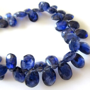 May include: A strand of dark blue gemstone beads, each bead is faceted and oval shaped. The beads are strung together to form a necklace or bracelet.