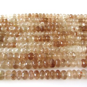 May include: A strand of faceted, translucent brown gemstone beads. The beads are round and have a slightly irregular shape. The beads are strung on a clear thread.