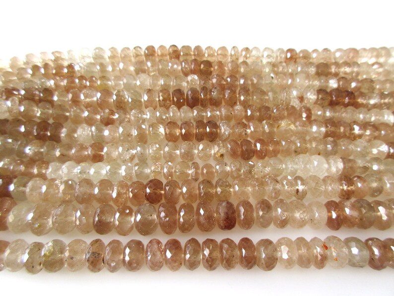 May include: A strand of faceted, translucent brown gemstone beads. The beads are round and have a slightly irregular shape. The beads are strung on a clear thread.