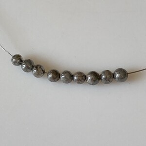 May include: A strand of round, gray beads with a speckled, metallic finish. The beads are strung on a silver wire.