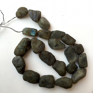 May include: A strand of dark grey labradorite gemstone beads, each bead is a natural, irregular shape, with some showing iridescent blue and green flashes.