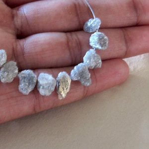 K&ouml;nnte beinhalten: Eine Str&auml;hne aus rauen, wei&szlig;en Diamantperlen, die auf einem silbernen Draht aufgef&auml;delt sind. Die Perlen sind in verschiedenen Gr&ouml;&szlig;en und Formen.