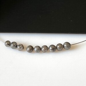 May include: A strand of silver-toned beads with a metallic finish. The beads are round and have a slightly textured surface.