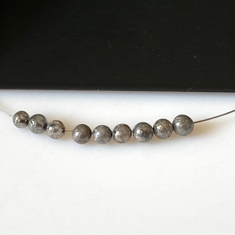 May include: A strand of silver-toned beads with a metallic finish. The beads are round and have a slightly textured surface.