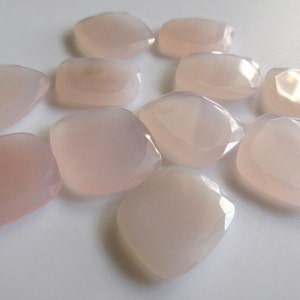 May include: A collection of ten pale pink, faceted, gemstone cabochons. The stones are smooth and polished, with a translucent appearance.