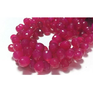 May include: A strand of pink faceted gemstone beads. The beads are teardrop shaped and have a glossy finish.