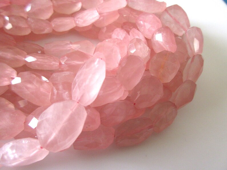 May include: A strand of pink rose quartz beads, each bead is faceted and oval shaped.