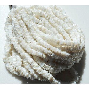 May include: A strand of white shell beads, each bead is a rectangular shape with a slightly irregular edge. The beads are stacked in a pile, showing the texture and color of the shell.