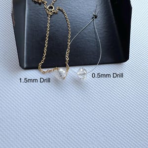 K&ouml;nnte beinhalten: Eine goldfarbene Metallkette mit einer facettierten, klaren Perle mit der Aufschrift 1.5mm Drill und eine klare Fadenschlaufe mit einer facettierten, klaren Perle mit der Aufschrift 0.5mm Drill. Die Perlen sind transparent, rund und texturiert.