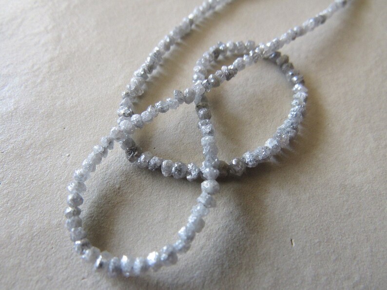 May include: A strand of rough, unpolished, gray diamonds strung together as a necklace. The diamonds are small and irregular in shape.