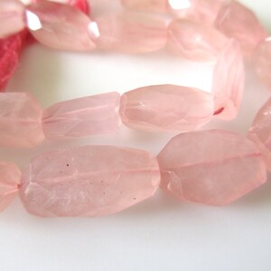 May include: A strand of pink rose quartz beads, each bead is faceted and has a slightly irregular shape. The beads are strung on a clear elastic cord.