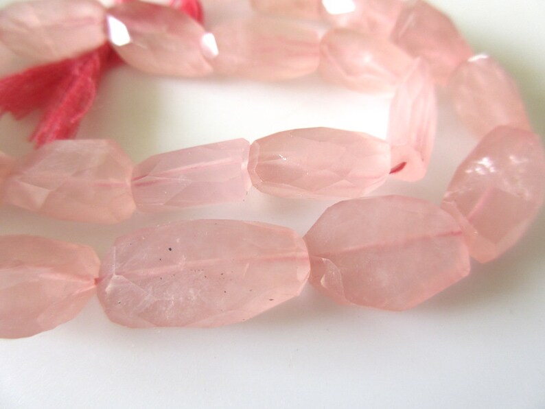 May include: A strand of pink rose quartz beads, each bead is faceted and has a slightly irregular shape. The beads are strung on a clear elastic cord.