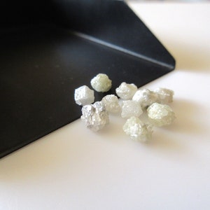 Puede incluir: Una colecci&oacute;n de peque&ntilde;os diamantes en bruto, blancos y verdes. Los diamantes est&aacute;n esparcidos sobre una superficie blanca.