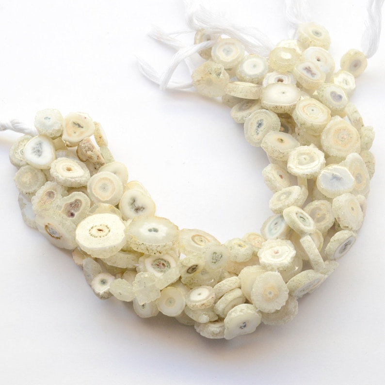 May include: A strand of white agate beads with a crystal-like appearance. The beads are round and flat, with a slightly rough texture. They are strung on a white cord.