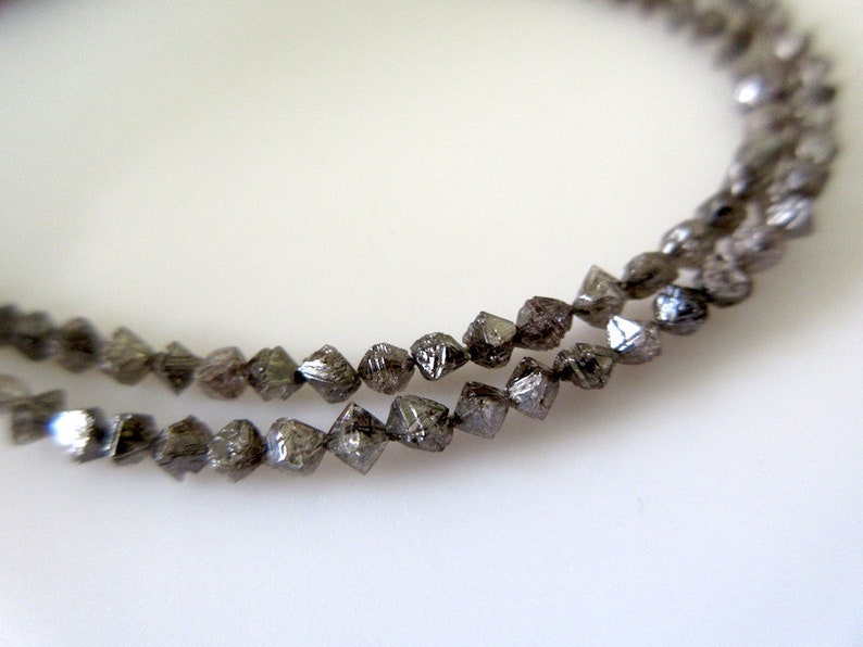 May include: A strand of dark grey, faceted diamond beads. The beads are small and have a rough, natural texture.