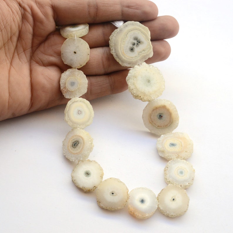 May include: A strand of white agate beads with a circular, flat shape and a crystal-like texture. The beads have a translucent appearance with a white and light brown color.