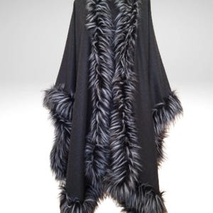 May include: A black cape with faux fur trim. The cape has a faux fur collar and trim along the front edges and cuffs. The faux fur is a mix of black and grey. The cape is displayed on a mannequin.
