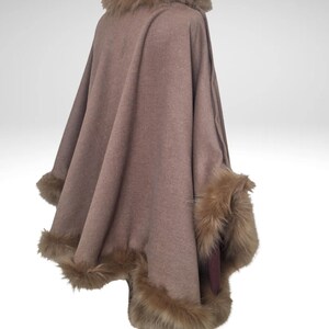 May include: A brown cape with faux fur trim around the collar and cuffs. The cape is displayed on a mannequin and has a flowing design. The faux fur is a lighter shade of brown than the cape.