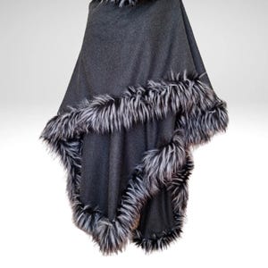 May include: A dark grey poncho with faux fur trim. The poncho has a faux fur collar and a border of black and white faux fur. The garment is displayed against a white background.