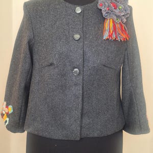 Handmade cropped wool alpaca jacket featuring intricate hand-embroidered floral details on the sleeves and a unique artisan brooch, showcasing exceptional craftsmanship.