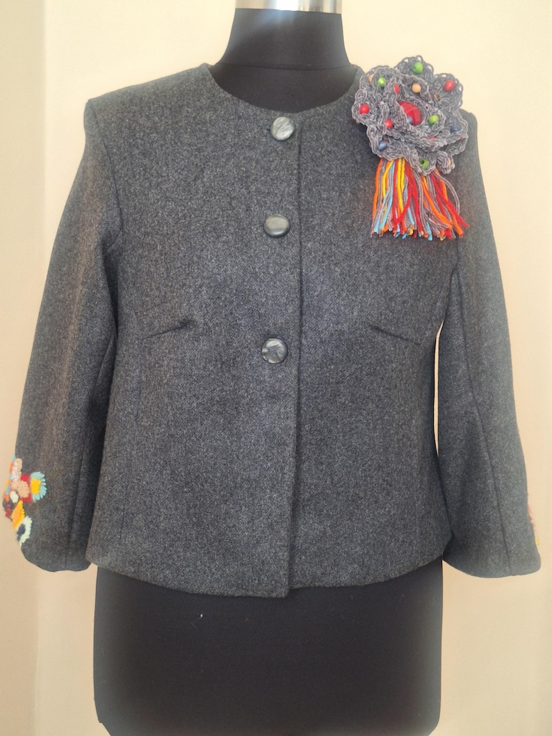 Handmade cropped wool alpaca jacket featuring intricate hand-embroidered floral details on the sleeves and a unique artisan brooch, showcasing exceptional craftsmanship.