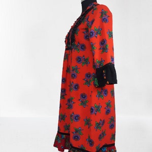 Side view of the red maxi dress with a floral print and black trim. The dress has long sleeves and a ruffled hem.