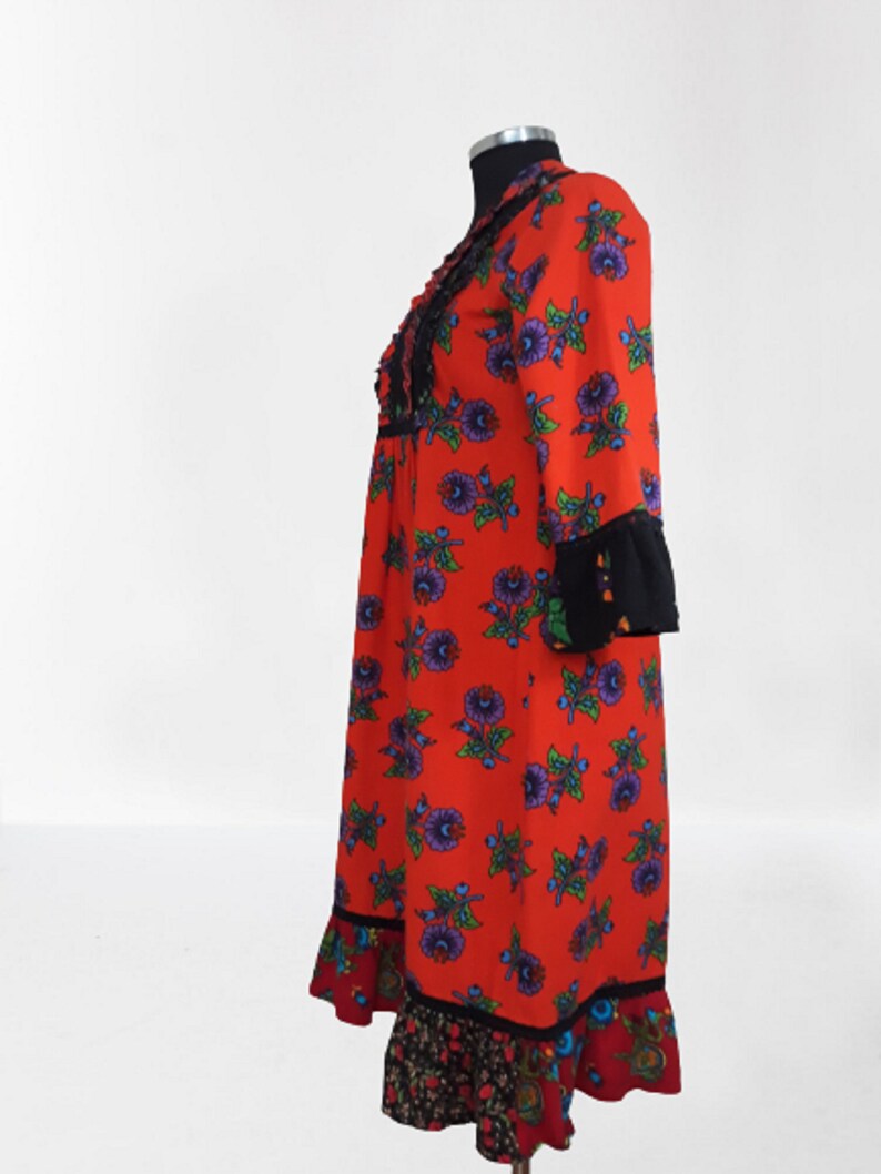Side view of the red maxi dress with a floral print and black trim. The dress has long sleeves and a ruffled hem.