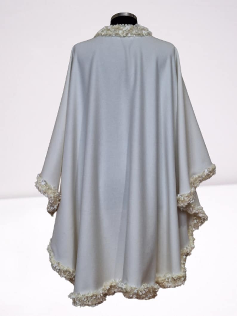 Back view of an off-white cashmere bridal cape with luxurious textured trim outlining the hem and neckline. Lightweight, flowing winter wedding shawl with a timeless vintage-inspired design.