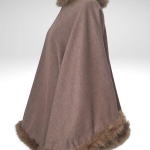 May include: A brown cape with faux fur trim around the collar and hem. The cape is displayed on a mannequin. The fur trim is a lighter shade of brown. The cape has a soft, flowing appearance.