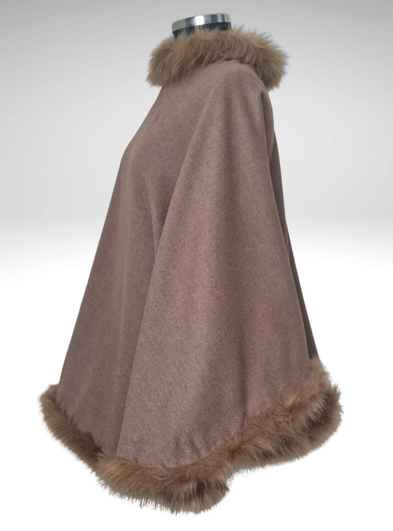 May include: A brown cape with faux fur trim around the collar and hem. The cape is displayed on a mannequin. The fur trim is a lighter shade of brown. The cape has a soft, flowing appearance.