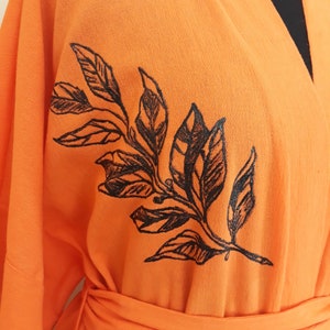 Puede incluir: Kimono naranja con un dise&ntilde;o floral negro. El kimono tiene manga larga y un cintur&oacute;n de atar.