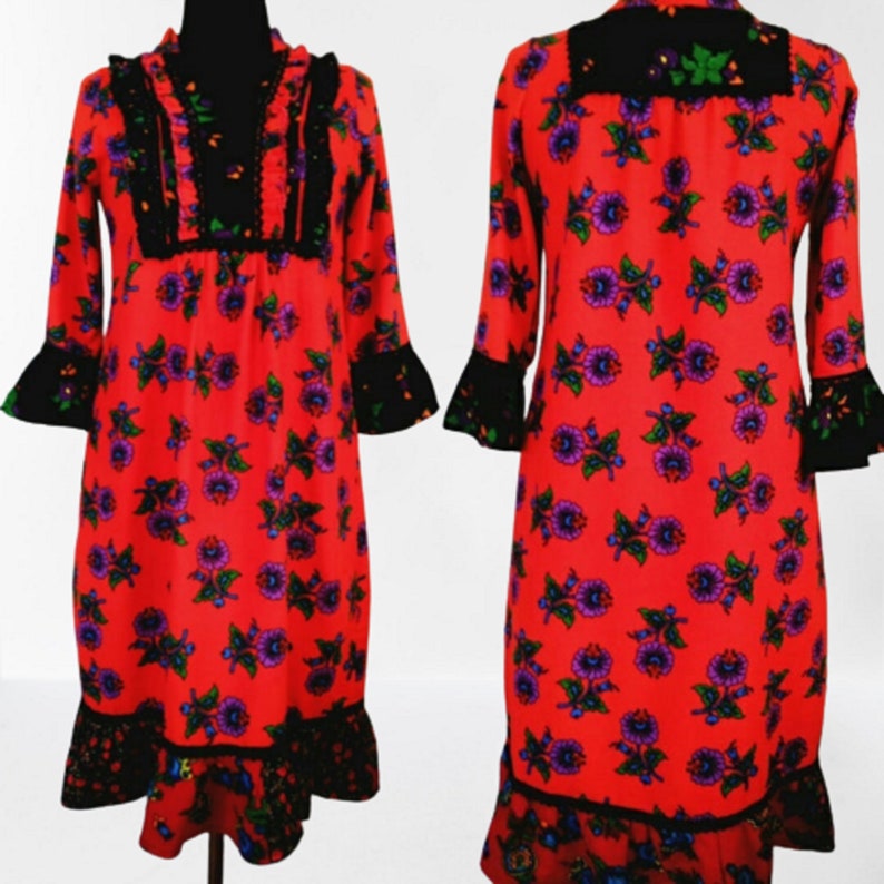 A red vintage style  dress with a floral print and black lace trim. The dress has long sleeves with bell cuffs and a gathered neckline.