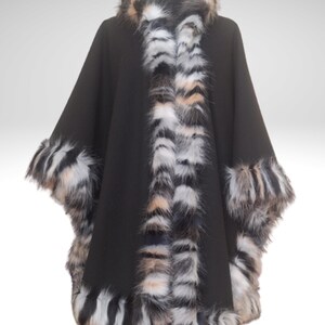 May include: A black cape with faux fur trim. The cape features a hood and is trimmed with a mix of black, white, and tan faux fur along the edges and collar. The cape is displayed on a mannequin.