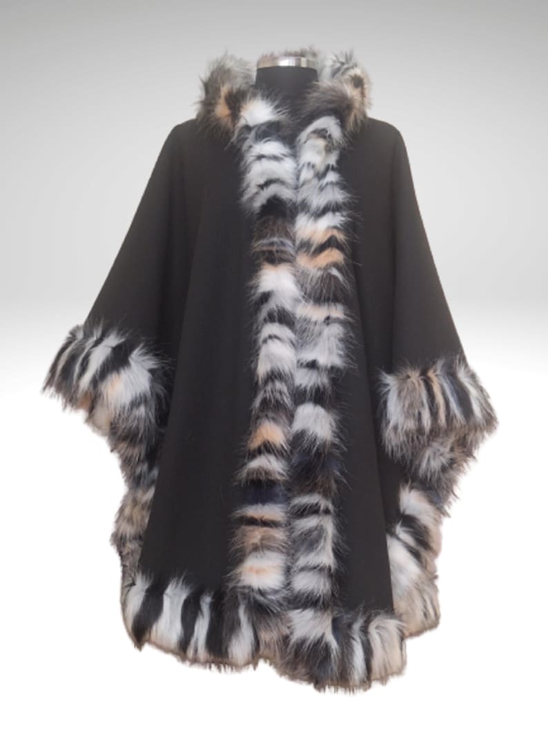May include: A black cape with faux fur trim. The cape features a hood and is trimmed with a mix of black, white, and tan faux fur along the edges and collar. The cape is displayed on a mannequin.