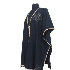 A black linen garment with gold trim and two gold embroidered flower designs, one on the chest and one on the lower left, displayed on a mannequin.