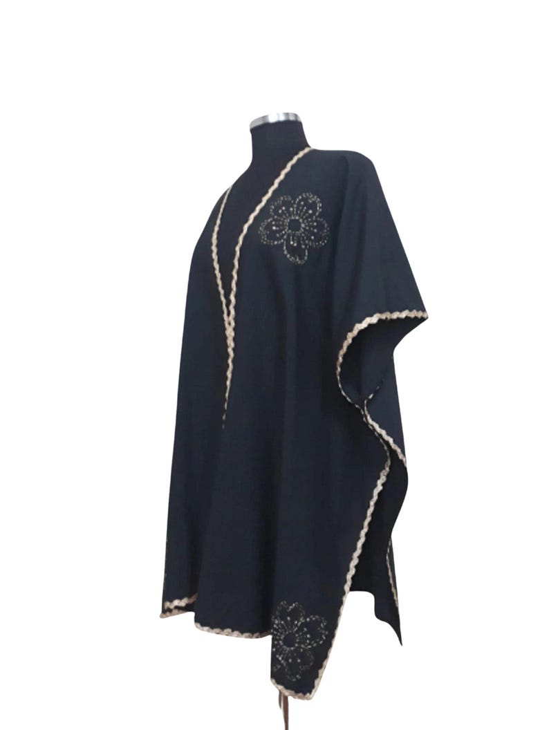 A black linen garment with gold trim and two gold embroidered flower designs, one on the chest and one on the lower left, displayed on a mannequin.