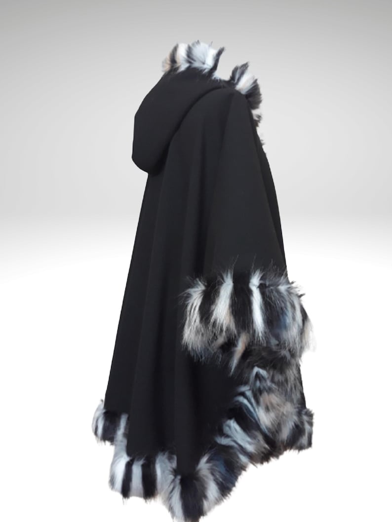 May include: A black hooded cape with faux fur trim. The cape features a hood and is trimmed with black, white, and gray faux fur along the hood, cuffs, and hemline. The cape is made of a soft, flowing fabric.
