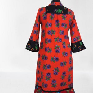 A red dress with a floral print and black trim. The dress has a ruffled hem and long sleeves.