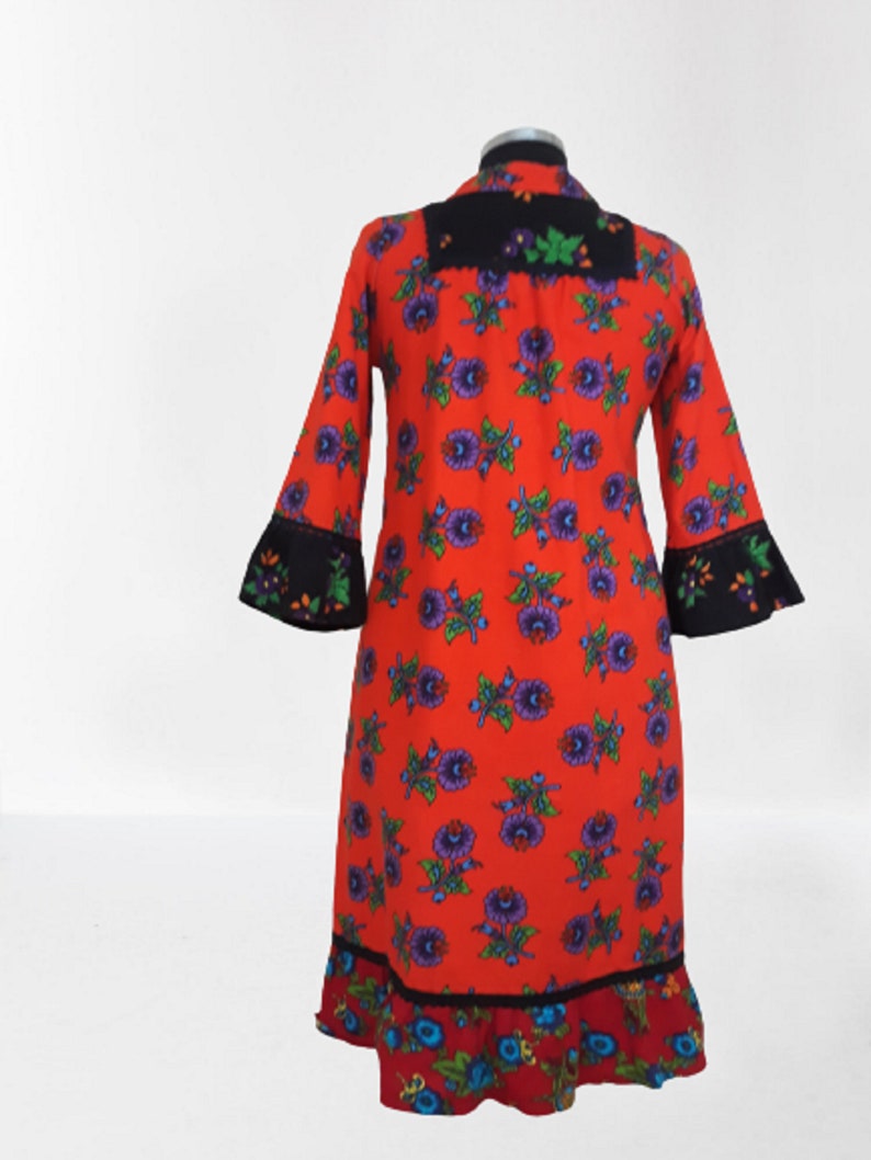 A red dress with a floral print and black trim. The dress has a ruffled hem and long sleeves.