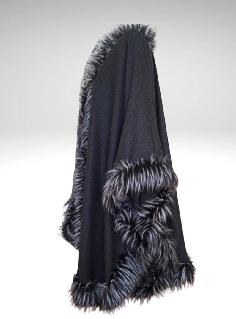 May include: A black cape with faux fur trim. The cape is made of a dark fabric and features a thick, fluffy trim in shades of grey and white along the edges and cuffs. The garment is draped, showcasing its shape.