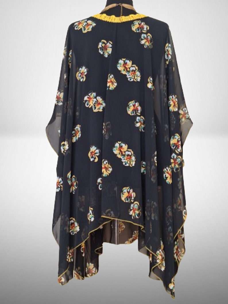 Puede incluir: Kimono negro de gasa transparente con estampado floral en amarillo, rojo y verde. El kimono tiene un ribete de crochet amarillo alrededor del escote.