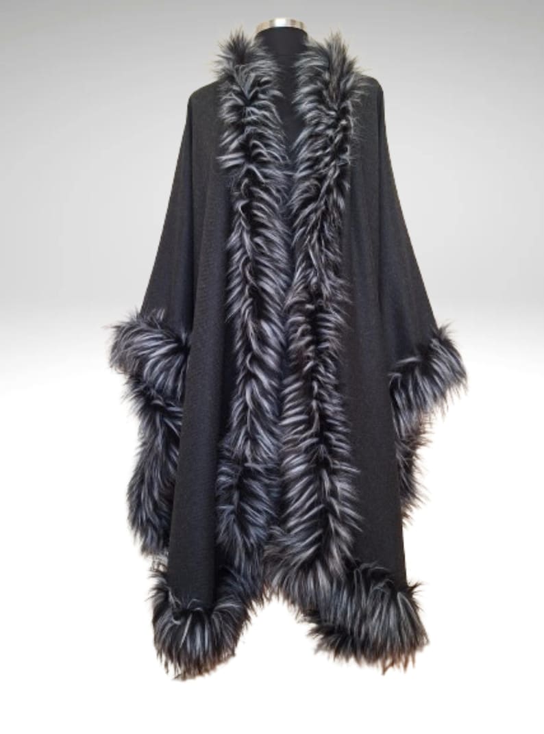 May include: A black cape with faux fur trim. The cape has a faux fur collar and trim along the front edges and cuffs. The faux fur is a mix of black and grey. The cape is displayed on a mannequin.