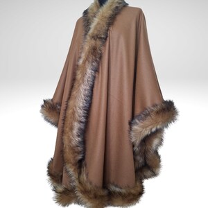 May include: A brown cape with faux fur trim. The cape features a wide collar and trim along the edges of the garment. The faux fur is a mix of brown and black. The cape is displayed on a mannequin.
