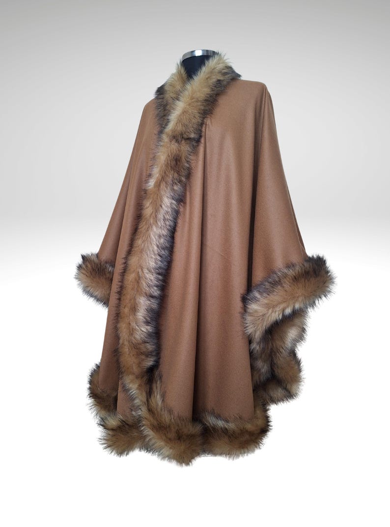 May include: A brown cape with faux fur trim. The cape features a wide collar and trim along the edges of the garment. The faux fur is a mix of brown and black. The cape is displayed on a mannequin.