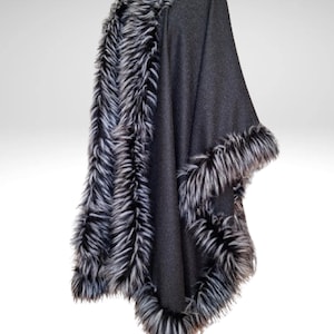 May include: A dark grey cape with faux fur trim in black and white. The cape is draped over a form, showing the design and texture of the fabric and trim. The fur trim is around the neckline and edges of the cape.