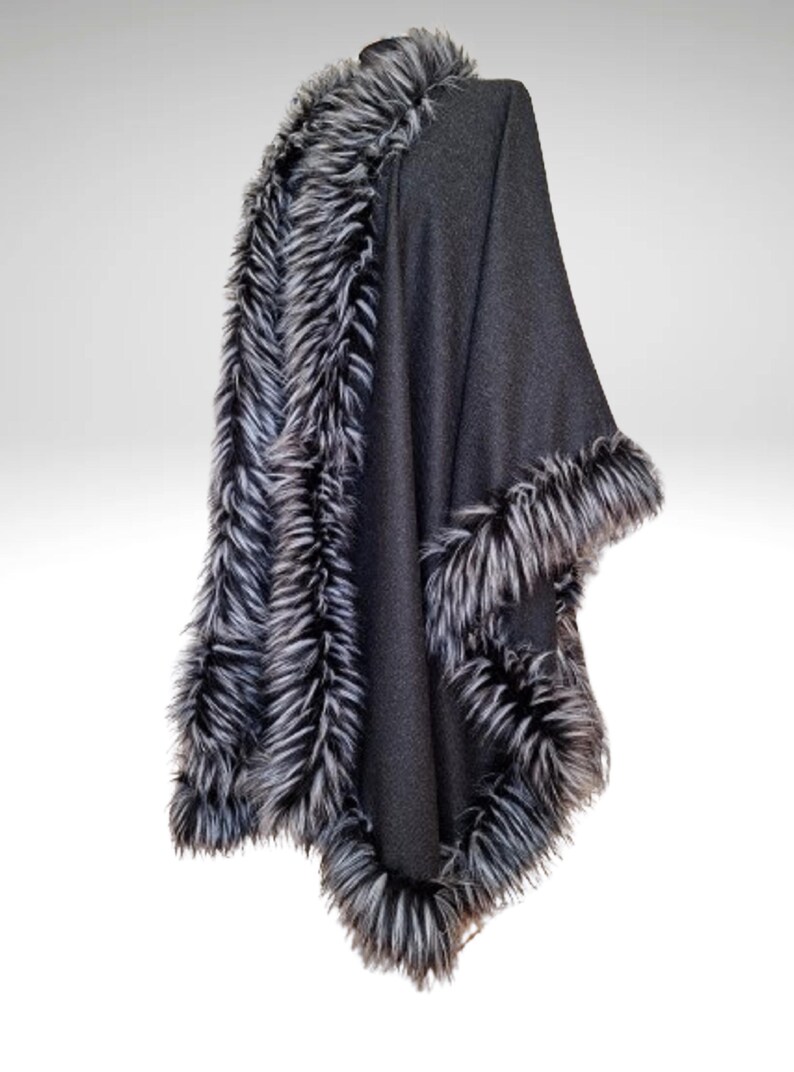 May include: A dark grey cape with faux fur trim in black and white. The cape is draped over a form, showing the design and texture of the fabric and trim. The fur trim is around the neckline and edges of the cape.